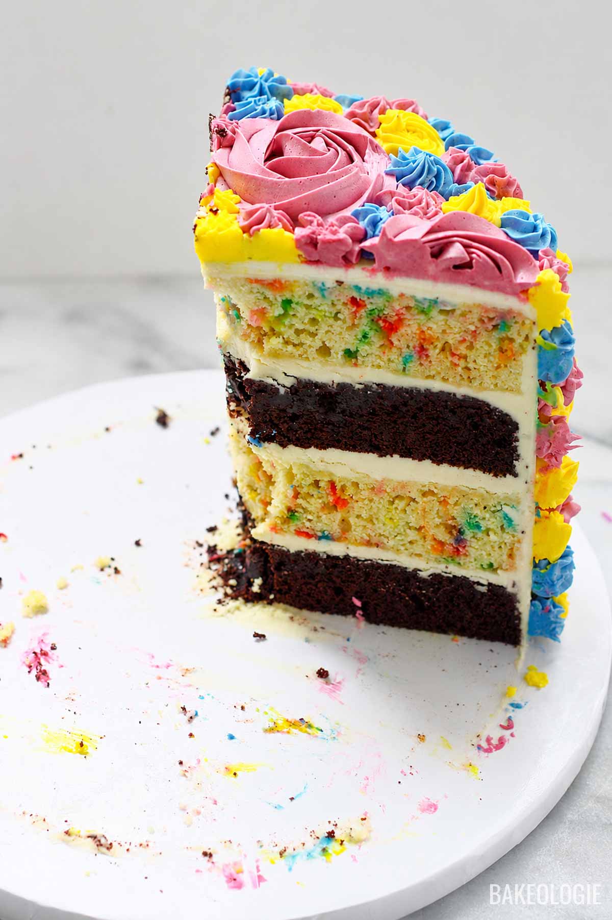 Tall slice of buttercream-frosted celebration cake with chocolate and vanilla sprinkle cake layers, decorated in pastel piping.