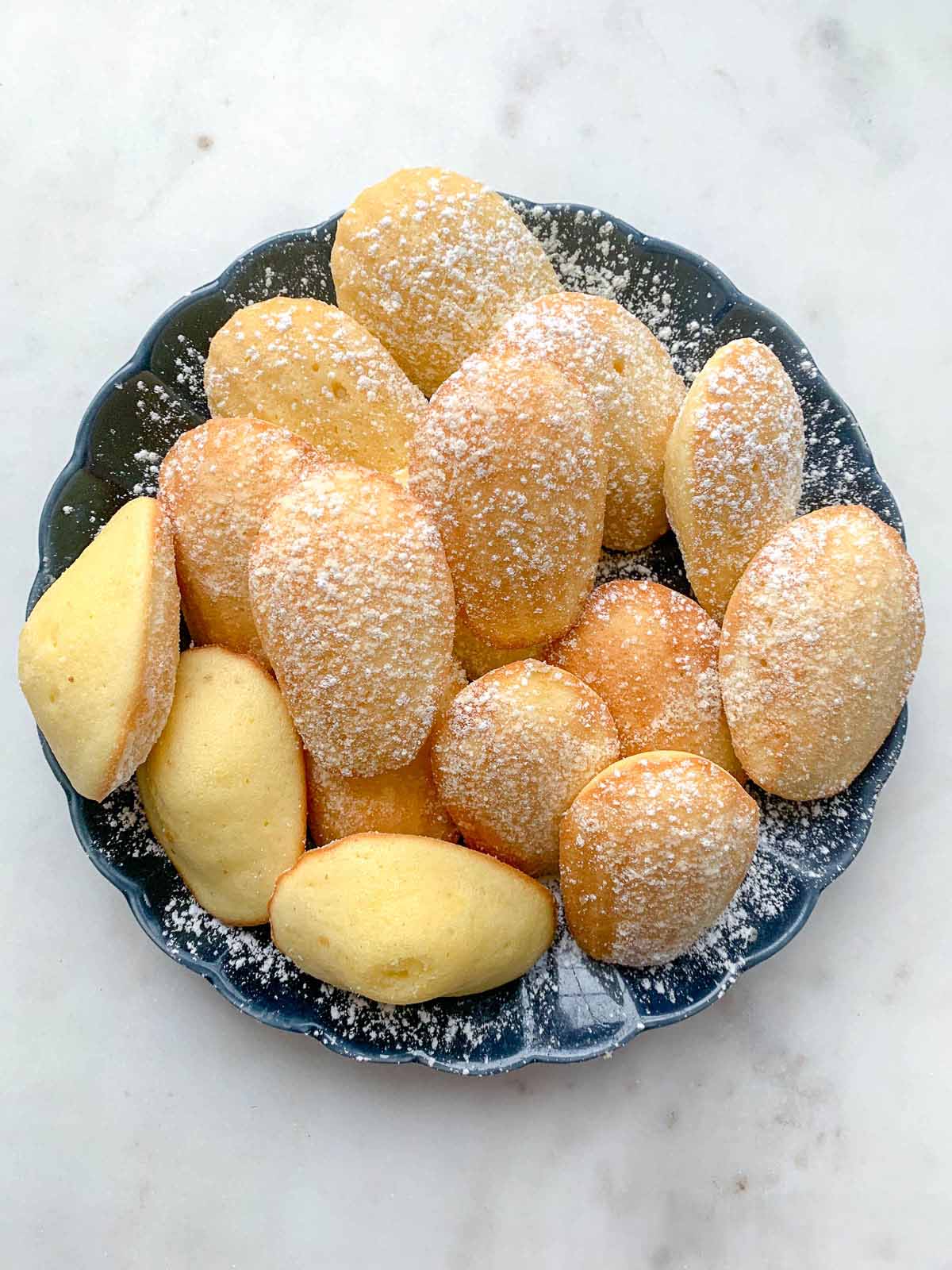 Buttery French madeleines with lightly crisp edges and soft centers, finished with a dusting of confectioners’ sugar.