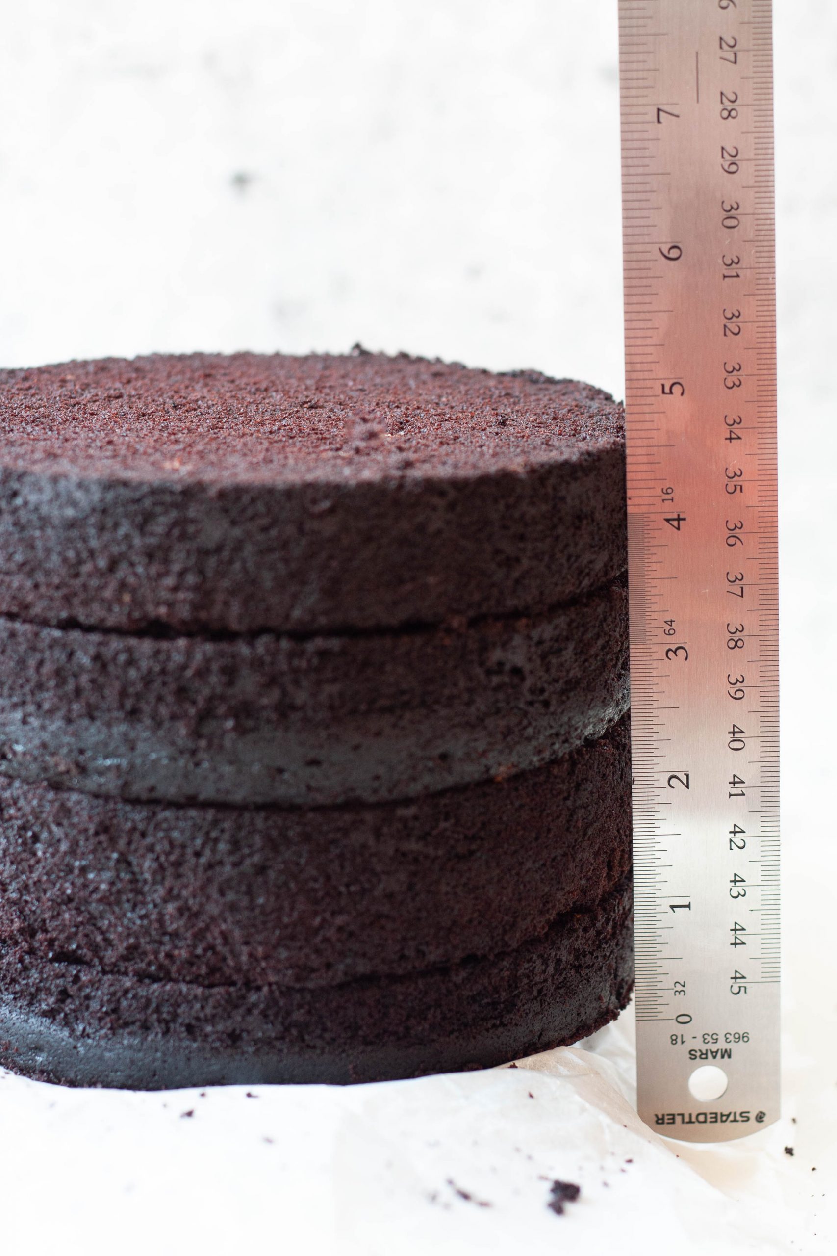 Three layers of moist chocolate cake stacked with a metal ruler beside them, showing a total height of about 5 inches.