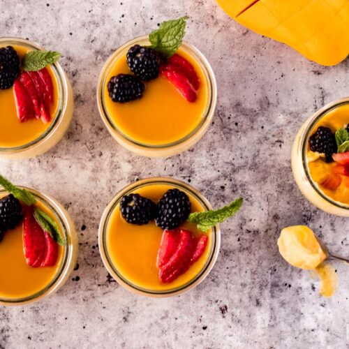 mango mousse served in individual glass containers with a spoon of creamy mango mousse