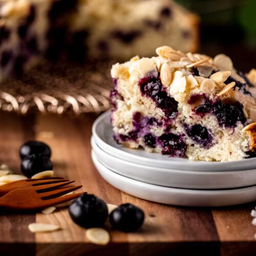 A close-up view of a sliced blueberry cake on a stack of small white plates - landscape photo