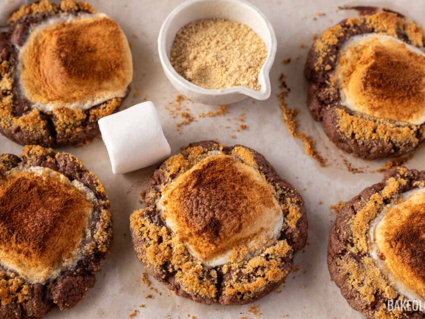 smores cookies on a baking sheet with large marshmallows and graham cracker crumbs