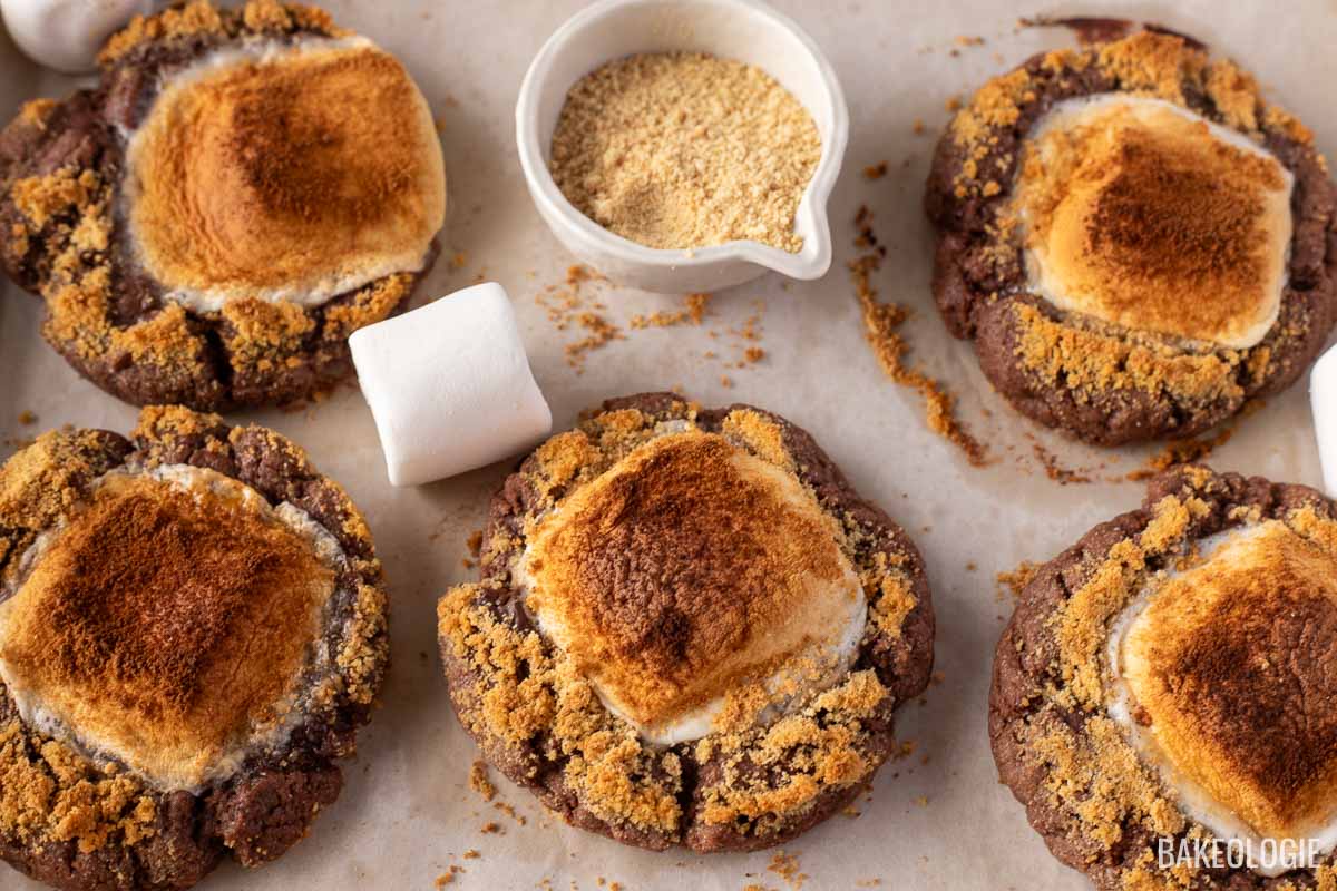 smores cookies on a baking sheet with large marshmallows and graham cracker crumbs