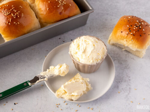 Whipped butter in a small bowl with buttered knife on the side and a piece of soft fluffy dinner roll.