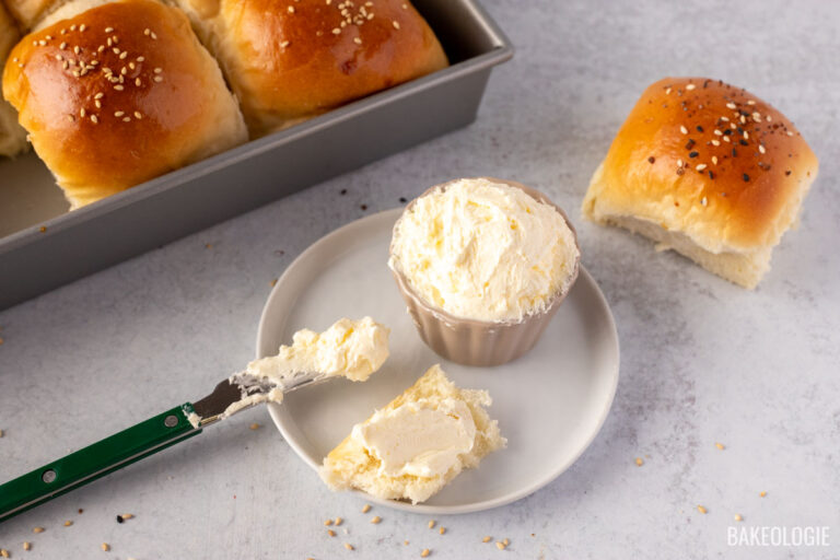 Whipped butter in a small bowl with buttered knife on the side and a piece of soft fluffy dinner roll.