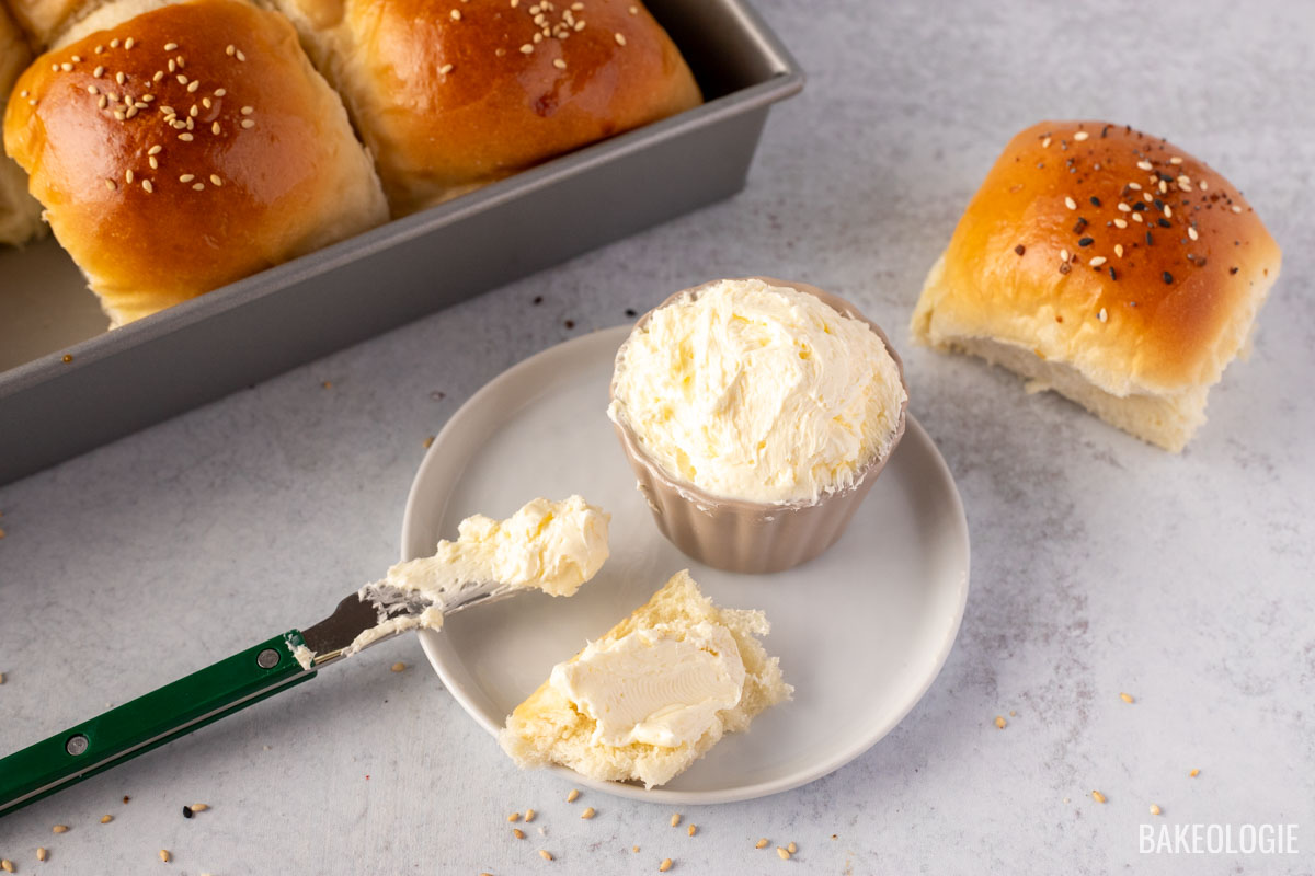 Whipped butter in a small bowl with buttered knife on the side and a piece of soft fluffy dinner roll.