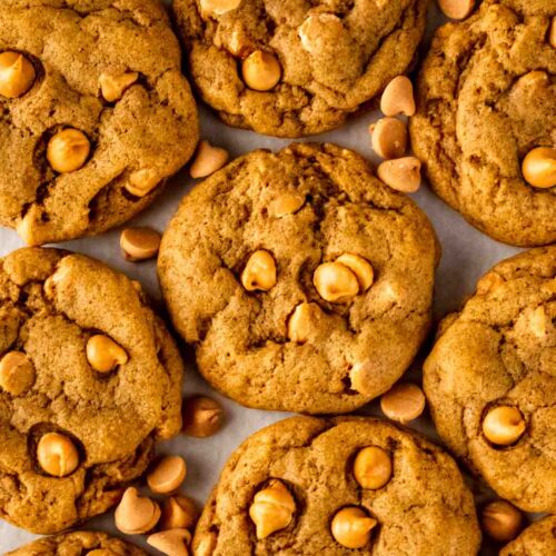 A close-up of several pumpkin butterscotch cookies arranged on parchment paper, highlighting their soft, chewy texture and studded with golden butterscotch chips.