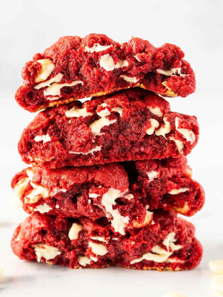 a stack of red velvet cookies cut in half showing the gooey, melty white chocolate.