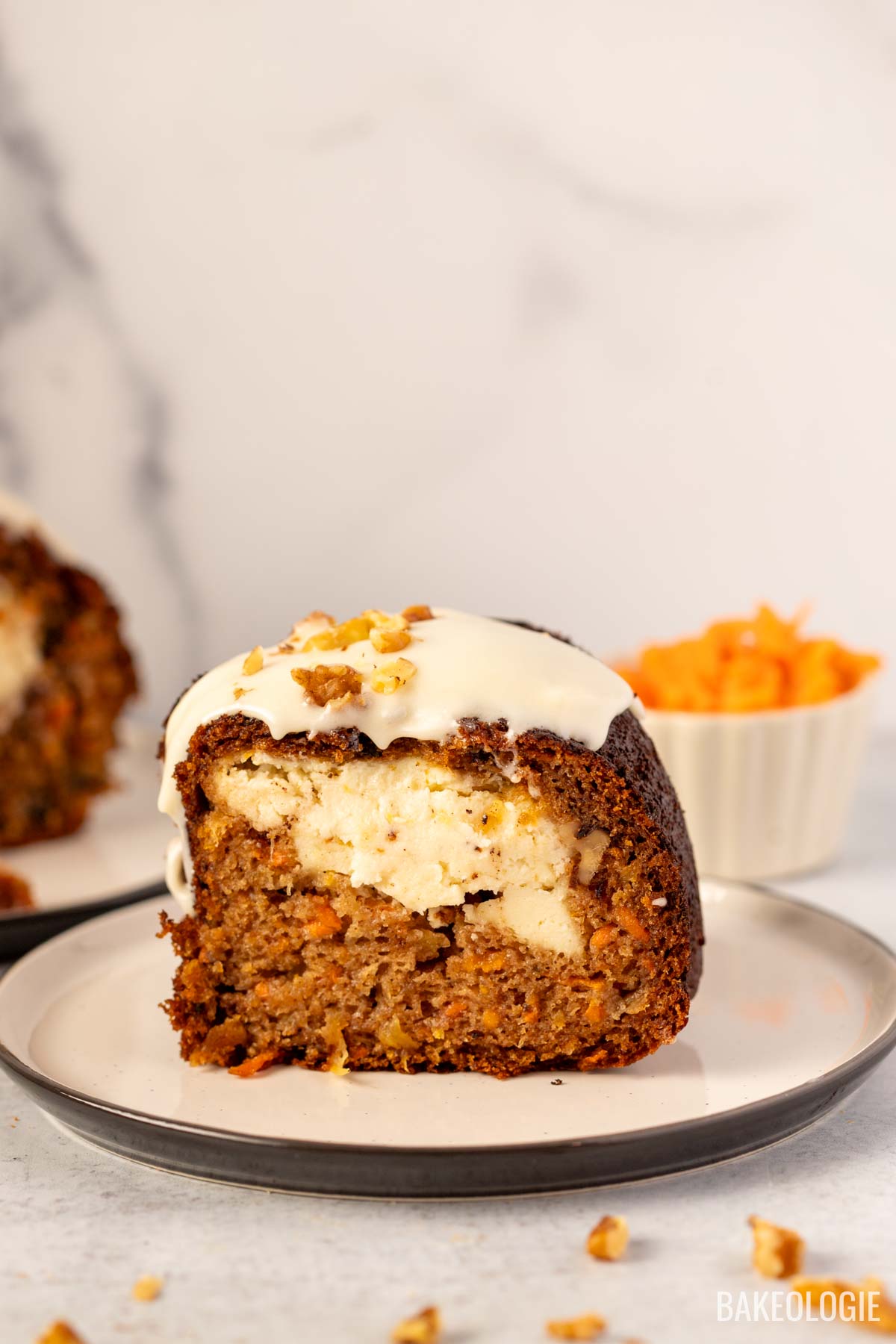 A close-up of a slice of carrot Bundt cake revealing the creamy cheesecake filling inside, topped with a cream cheese glaze and sprinkled with chopped walnuts.