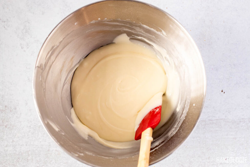 Spreading cream cheese glaze over a carrot Bundt cake with a spatula, letting it cascade down the sides.