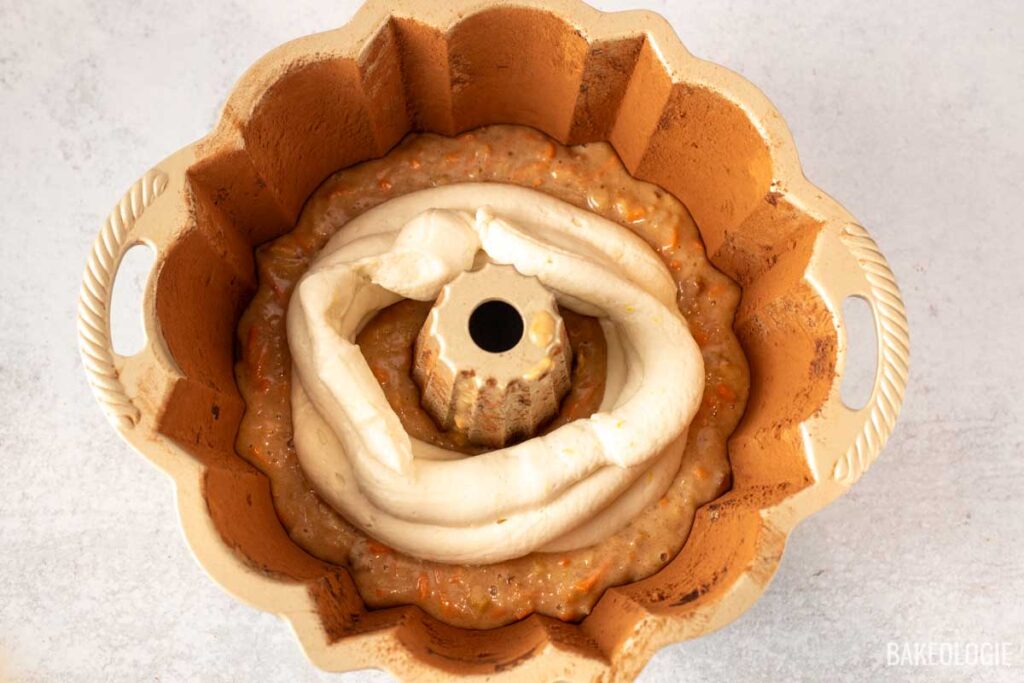 A piping bag filled with cheesecake filling is used to pipe a ring of filling over the carrot cake batter in the Bundt pan.