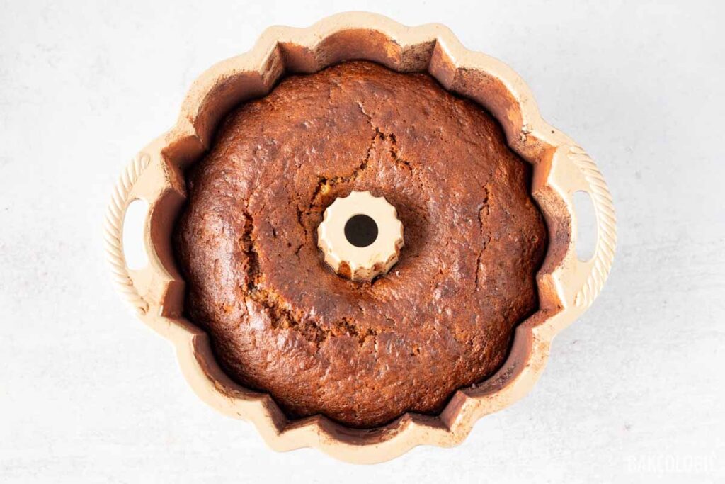 Overhead view of a fully baked carrot Bundt cake, with a golden-brown top and cracks around the edges, still in the Bundt pan.