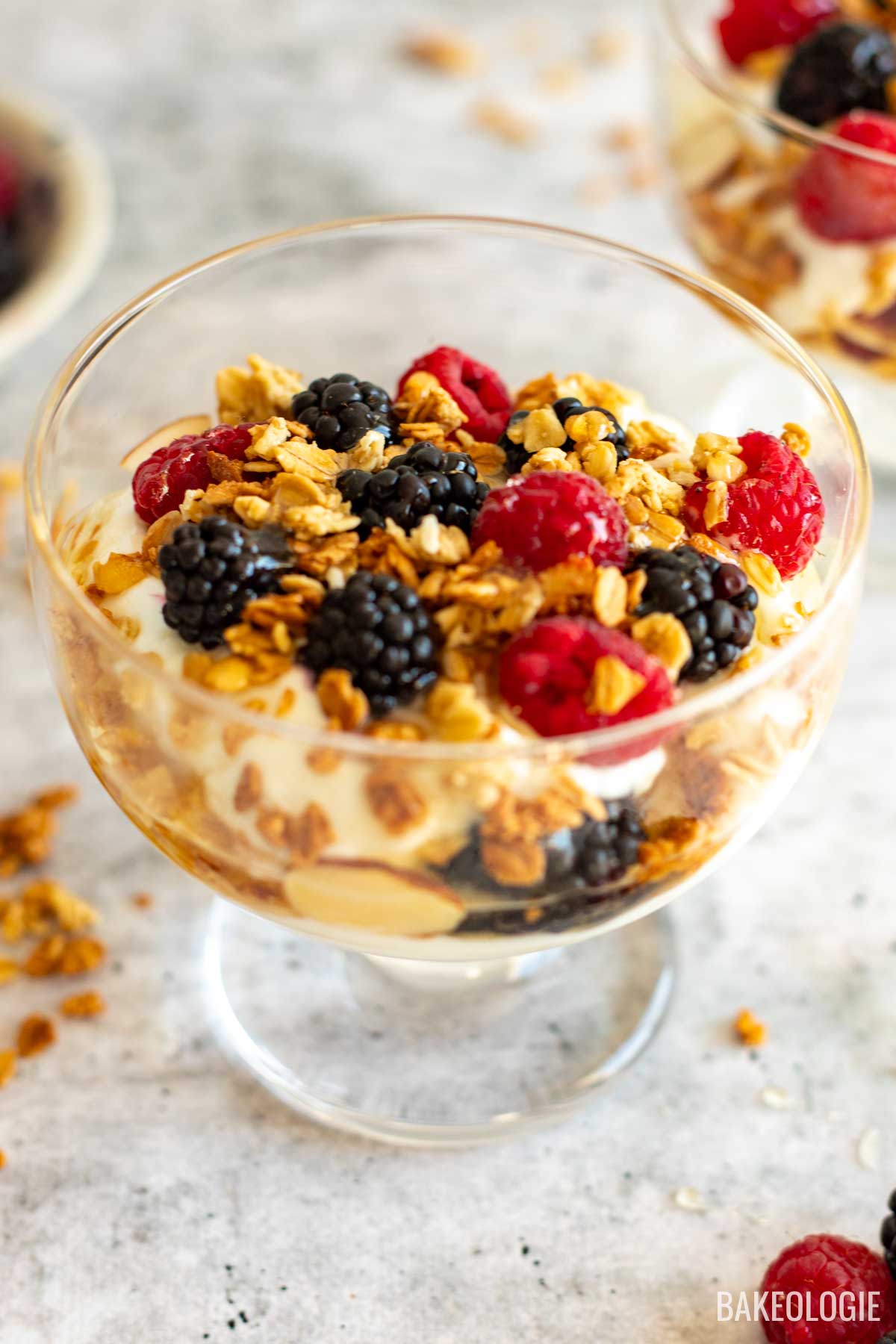 Close-up side view of a Greek yogurt parfait served in a clear glass, highlighting layers of creamy yogurt, golden granola clusters, and vibrant fresh blackberries and raspberries.