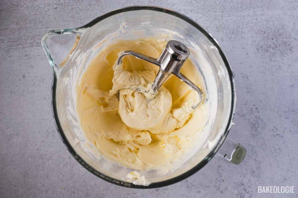 Glass mixing bowl with smooth, whipped cream cheese mixture and a paddle attachment, ready for the next step in making Blueberry Crumble Cheesecake Bars.