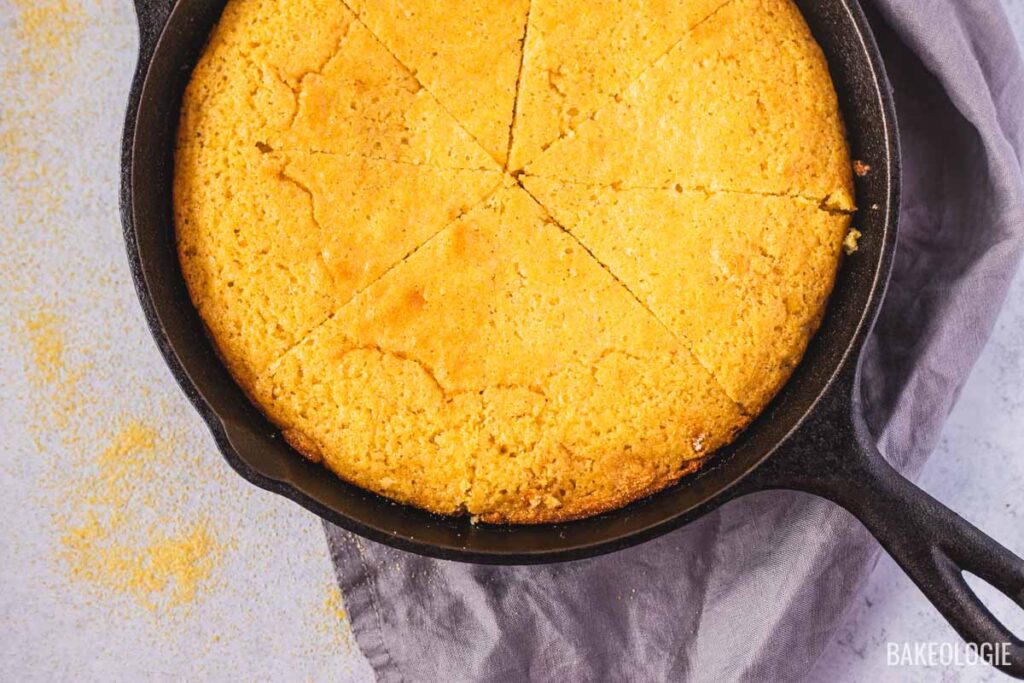 Cast iron skillet cornbread recipe with golden brown crust, sliced into wedges showing crispy edges and tender crumb.