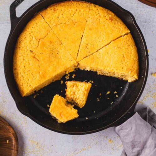 Cast iron skillet cornbread with crispy edges and moist tender crumb, sliced into wedges.