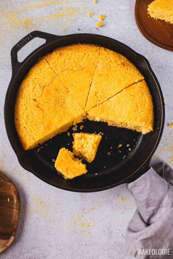 Cast iron skillet cornbread with crispy edges and moist tender crumb, sliced into wedges.