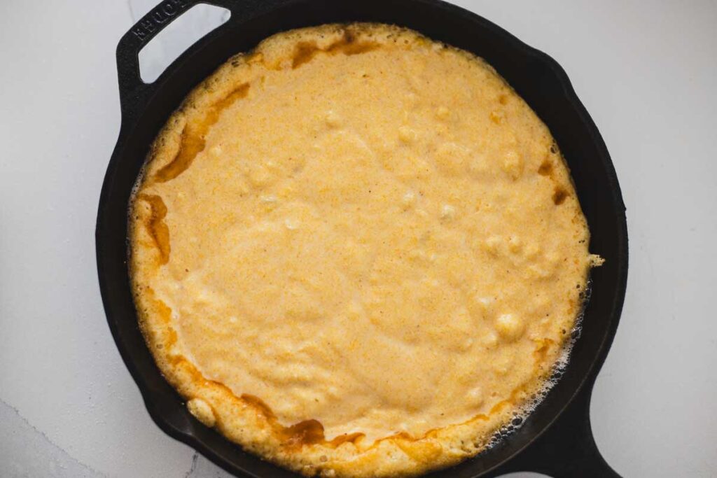 Cornbread batter poured into a hot cast iron skillet, edges sizzling before baking.