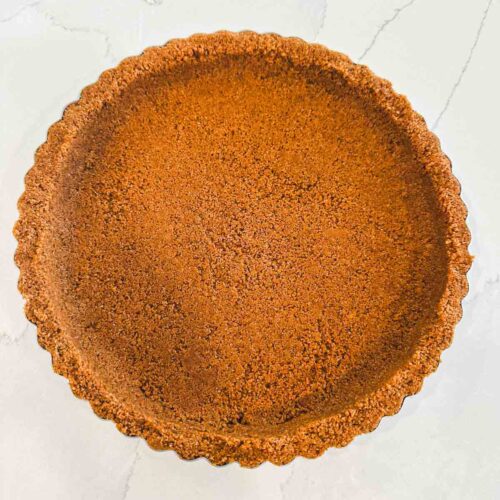 Baked graham cracker crust in a fluted 9-inch tart pan with golden brown edges and a smooth, even crumb base.