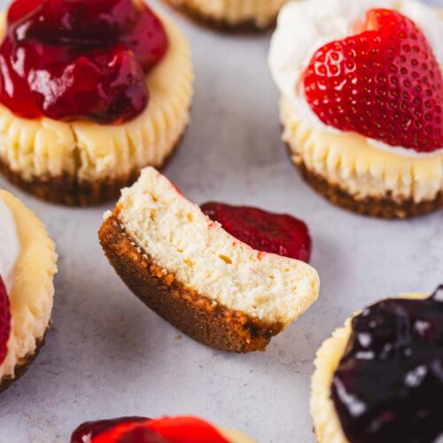 Mini cheesecakes baked in a muffin tin with different toppings like strawberry, cherry, and blueberry for a variety of flavors.
