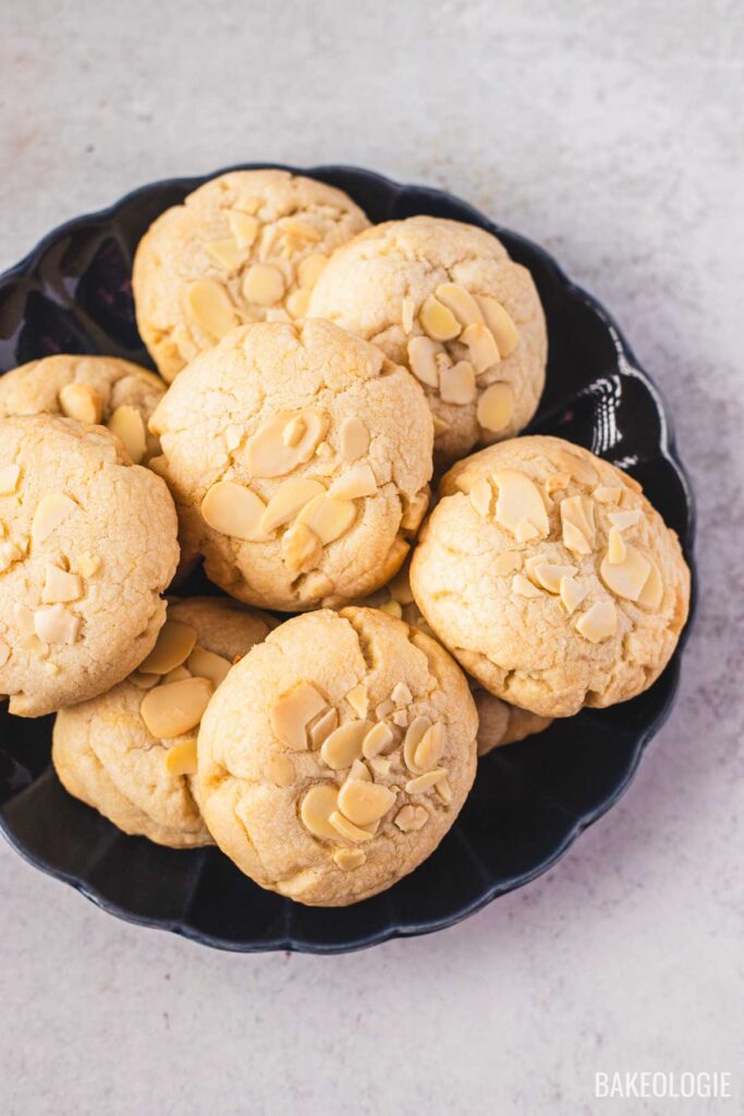 A plate of freshly baked almond croissant cookies topped with sliced almonds, showing their golden color and soft, thick texture.