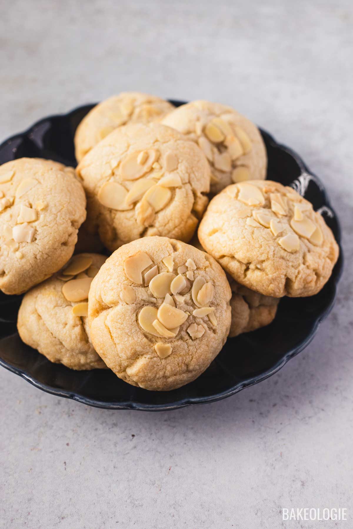 A plate of golden almond croissant cookies topped with sliced almonds, showing their soft, thick texture and slightly cracked tops.