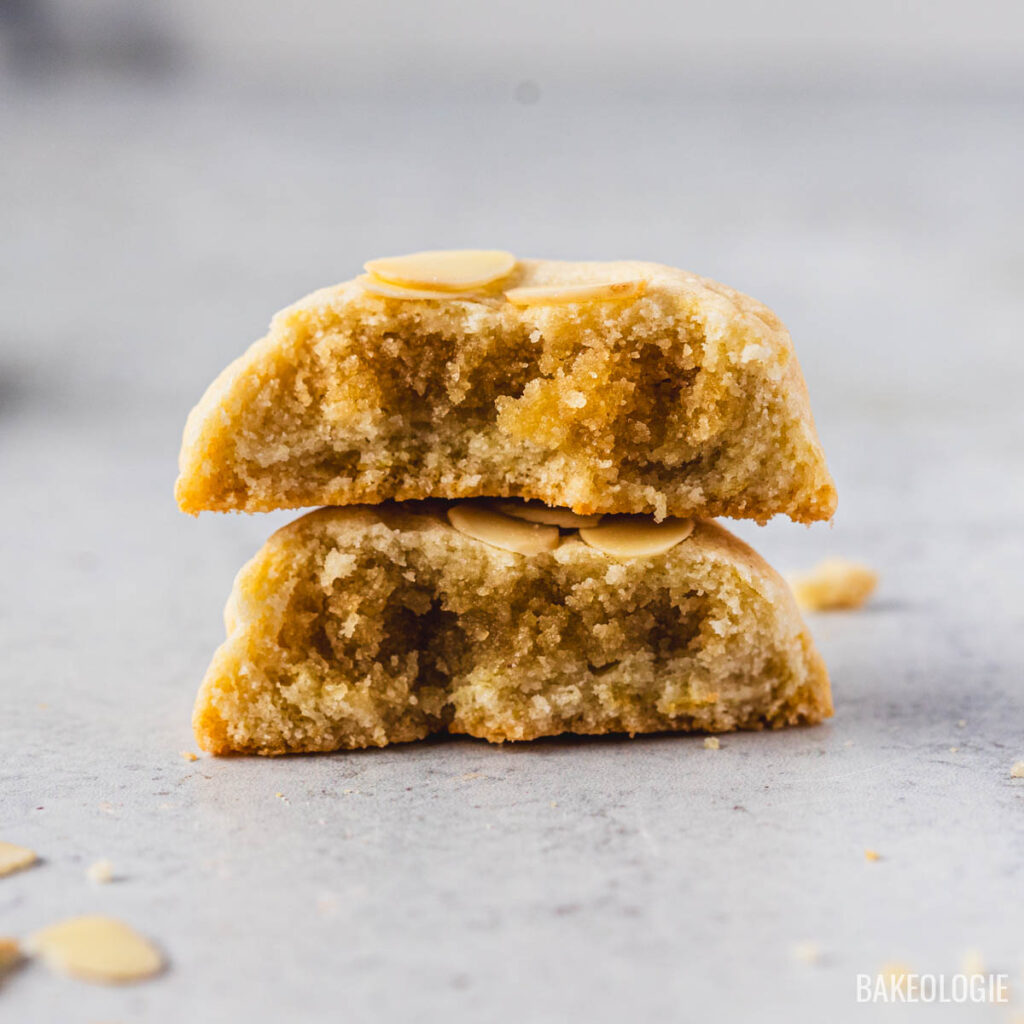 Close-up of a halved almond croissant cookie stacked to reveal its gooey almond filling and chewy center, topped with sliced almonds.
