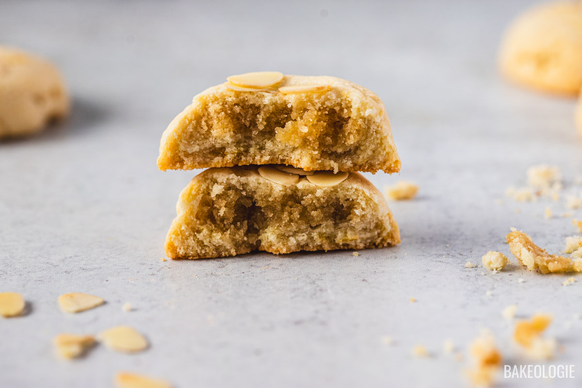 Close-up of a halved almond croissant cookie stacked to reveal its gooey almond filling and chewy center, topped with sliced almonds.