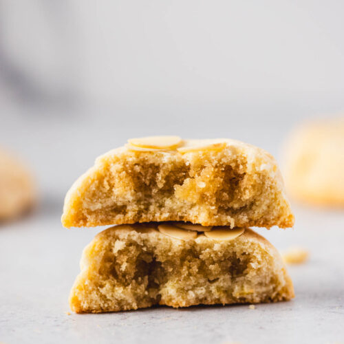 Close-up of a halved almond croissant cookie stacked to reveal its gooey almond filling and chewy center, topped with sliced almonds.