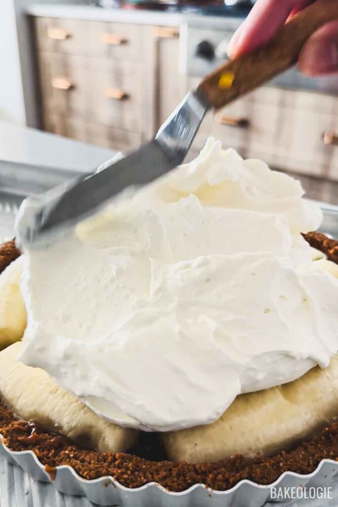 Spreading whipped cream over bananas to assemble Banoffee Pie