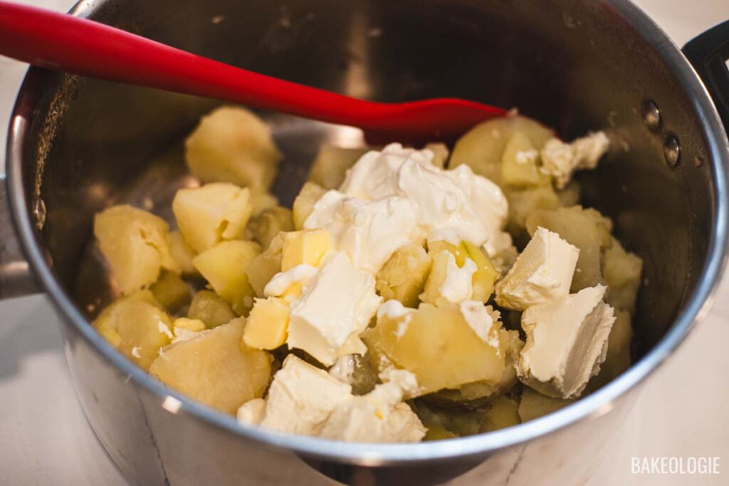A pot filled with boiled potatoes, sour cream, butter, and cream cheese, ready to be mashed together.
