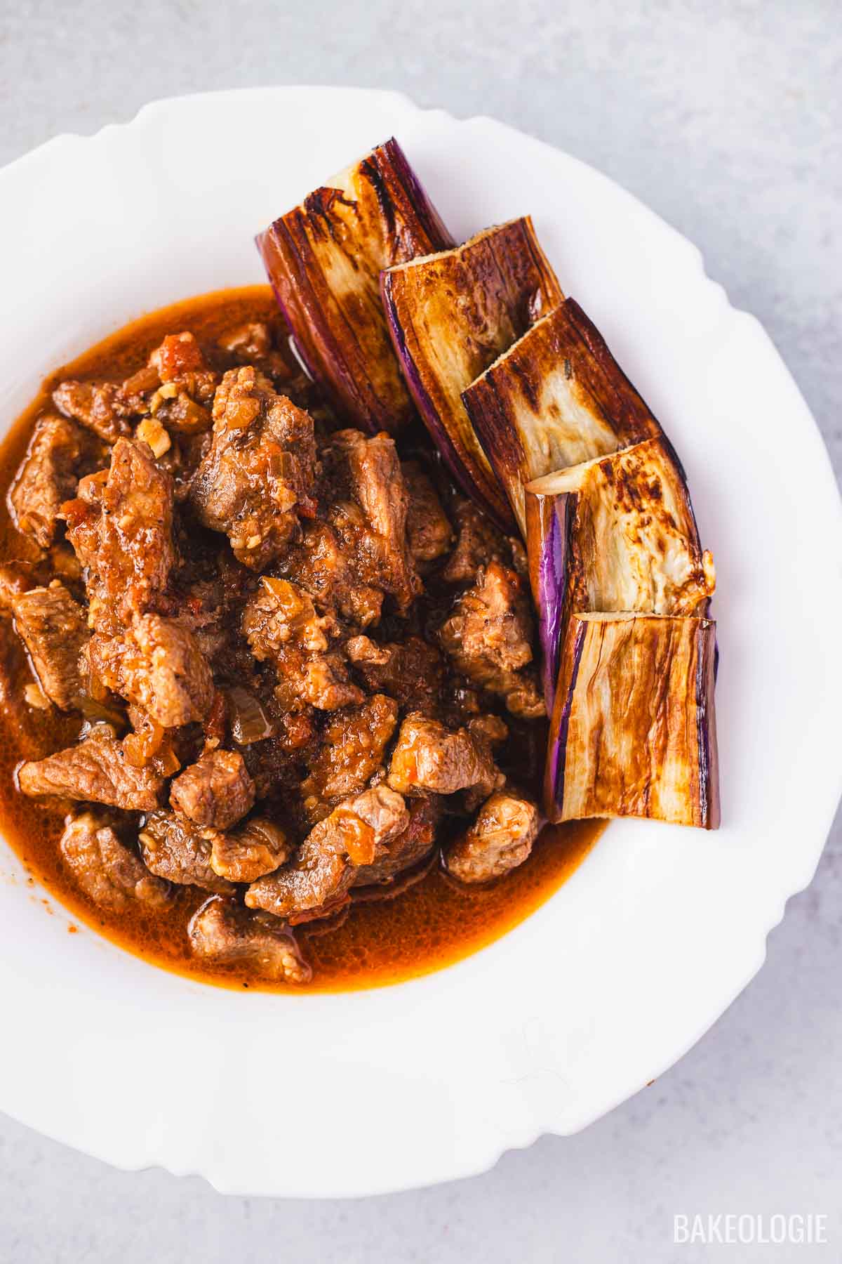 Overhead shot of binagoongang baboy in a white bowl, with rich shrimp paste sauce and fried eggplant slices.