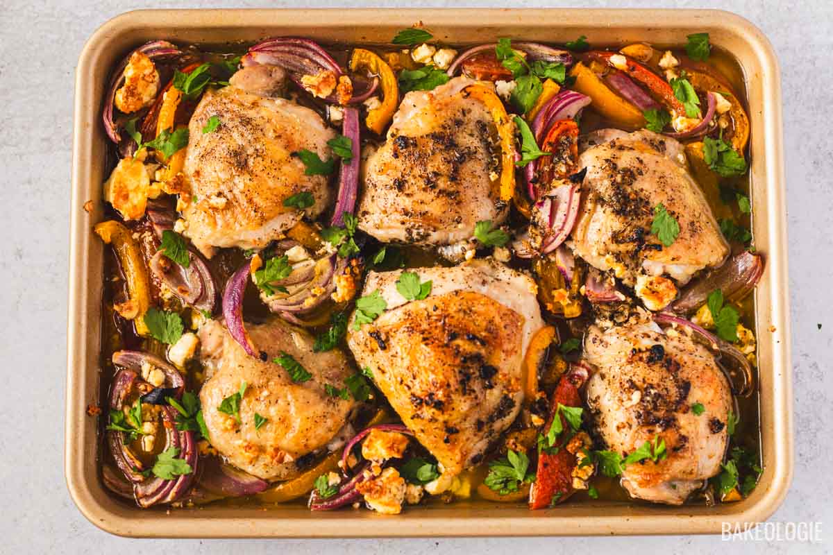 Sheet pan Greek chicken with crispy skin, roasted bell peppers, red onions, and feta, baked until golden and garnished with fresh parsley.