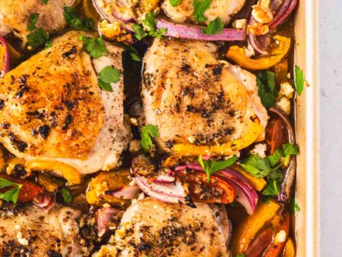 Close-up of sheet pan Greek chicken thighs surrounded by roasted vegetables, lemon slices, and feta for an easy one-pan Mediterranean dinner.