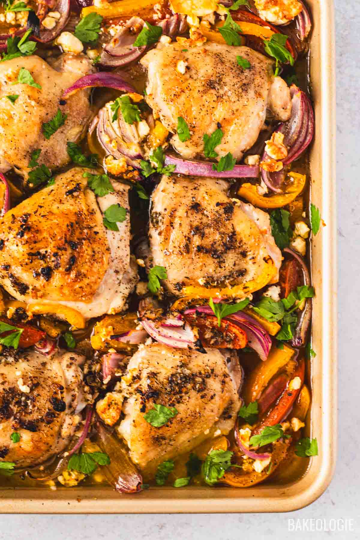 Close-up of sheet pan Greek chicken thighs surrounded by roasted vegetables, lemon slices, and feta for an easy one-pan Mediterranean dinner.