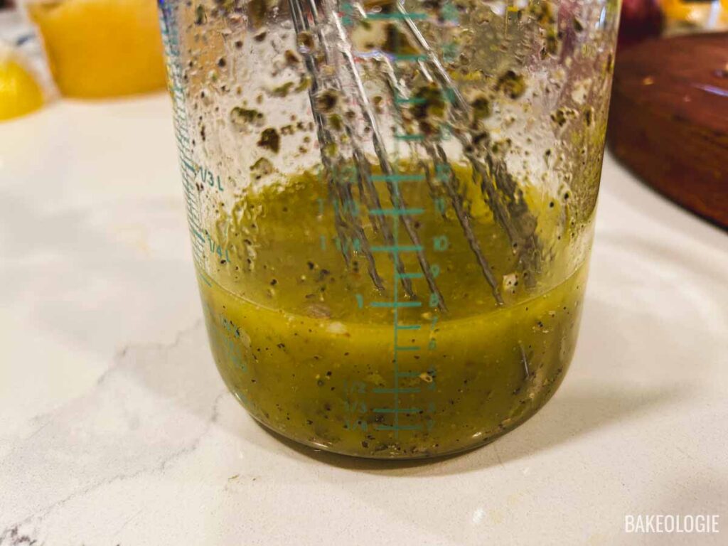 Whisking together lemon juice, olive oil, garlic, oregano, salt, and pepper to make the Greek chicken marinade in a measuring cup.