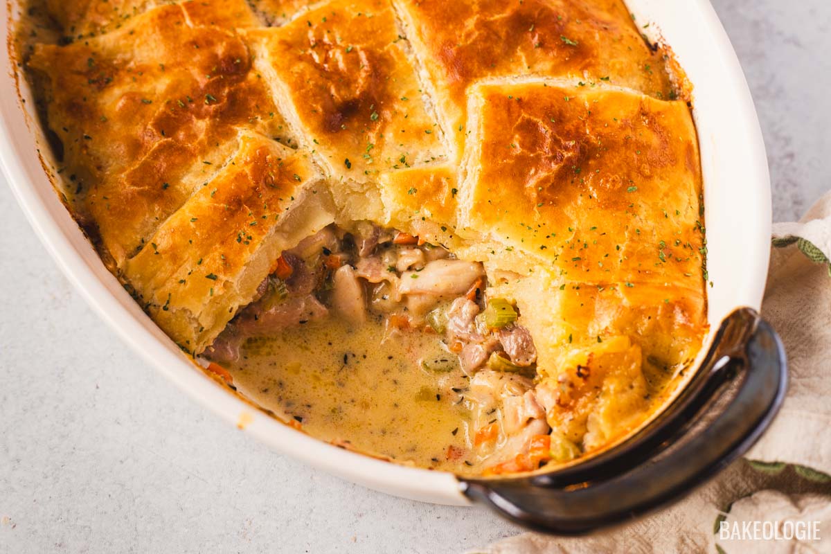 Overhead view of a baked chicken pot pie with flaky puff pastry squares and creamy chicken filling in a white oval dish.