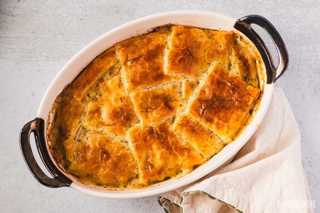 Golden brown chicken pot pie with puff pastry squares freshly baked in a white oval dish, showing a flaky, crisp crust on top of creamy chicken filling.