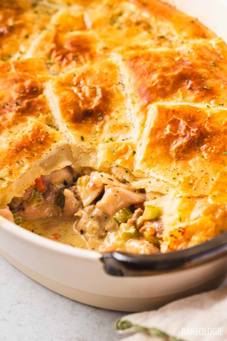 Close-up of a creamy chicken pot pie topped with golden puff pastry squares in a white baking dish, showing the tender chicken and vegetables in a rich sauce.