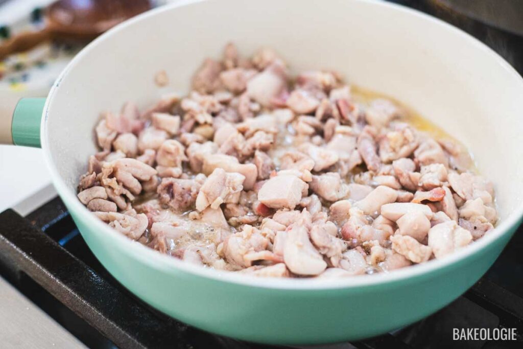 Chicken and bacon pieces cooking in a skillet until golden, the first step in making creamy chicken pot pie filling.