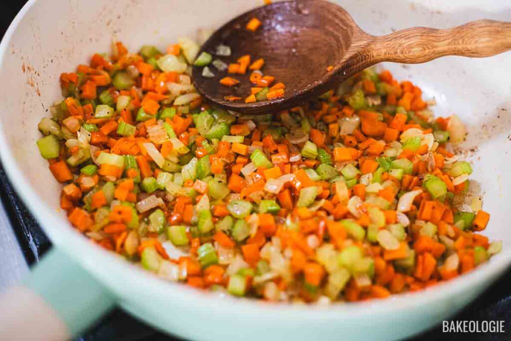 Diced onions, celery, and carrots being sautéed in butter in a skillet for chicken pot pie with puff pastry.