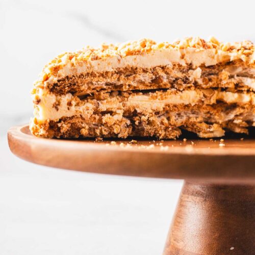 A sliced Sans Rival cake showing its crisp cashew meringue layers and creamy buttercream, set on a wooden cake stand.