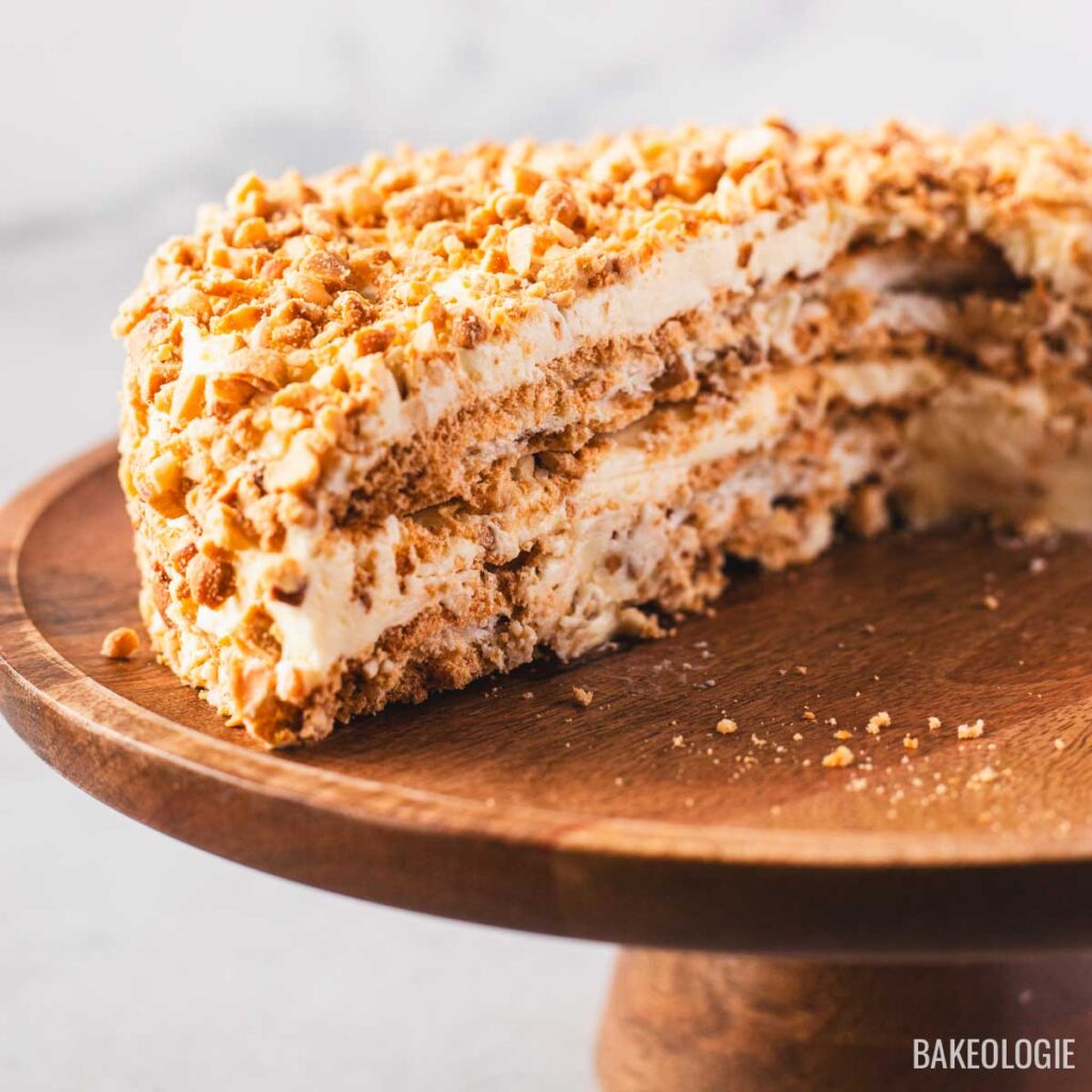 A partially sliced Sans Rival cake revealing the stacked cashew meringue and buttercream layers, sitting on a wooden cake stand.