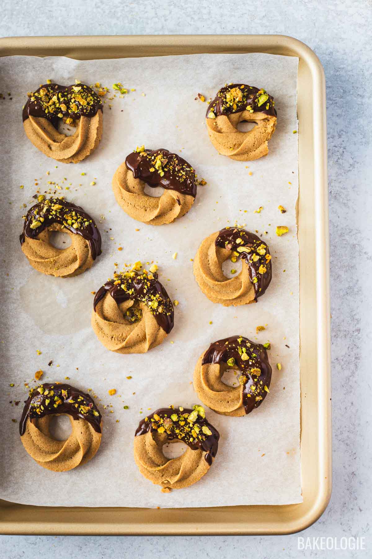 Chocolate-dipped coffee swirl cookies topped with chopped pistachios, arranged on a parchment-lined baking sheet.
