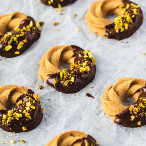 Coffee swirl cookies dipped in chocolate and topped with chopped pistachios, arranged on a sheet of parchment paper.