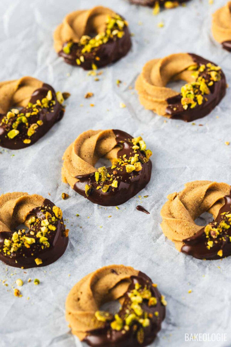Coffee swirl cookies dipped in chocolate and topped with chopped pistachios, arranged on a sheet of parchment paper.