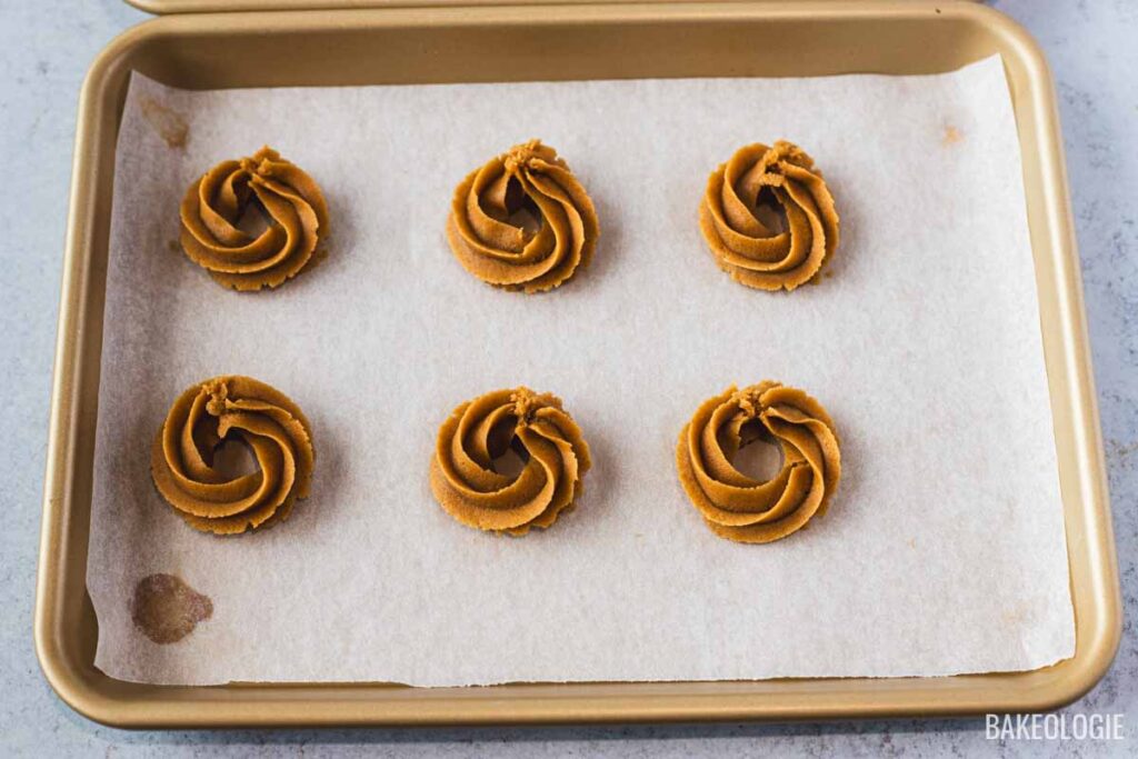 Freshly piped coffee cookie swirls on a parchment-lined baking sheet, ready to be chilled.