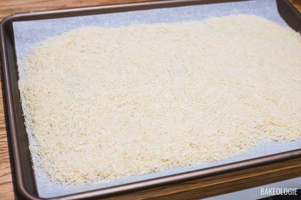 Dried kataifi strands spread in an even layer on a parchment-lined baking sheet, ready to be toasted in the oven.