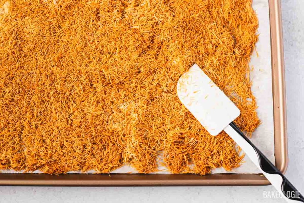 Golden, deeply toasted kataifi strands on a baking sheet, with a spatula showing the crisp, flaky texture.