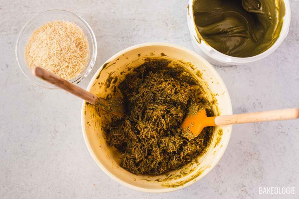 Bowl of pistachio kataifi filling being mixed until fully combined, with toasted kataifi strands and pistachio cream visible in the background.
